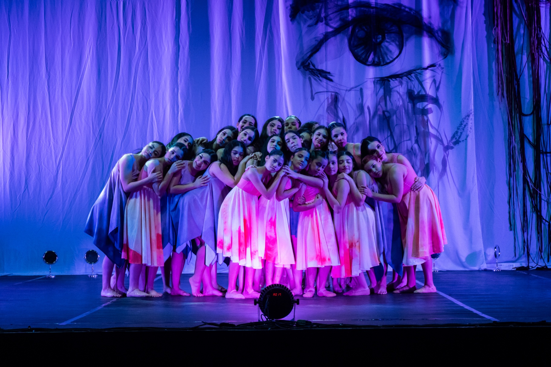 Alumnas de DANZAR abrazadas en escena bajo luces violetas y rosas